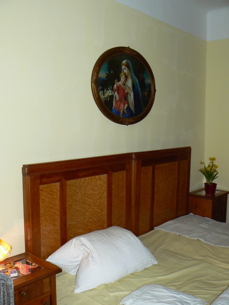 Gelbes Gästezimmer im Gasthaus zur Hinterbrühl mit historischem Doppelbett, Nachtkästchen und zeittypischer Wandgestaltung.