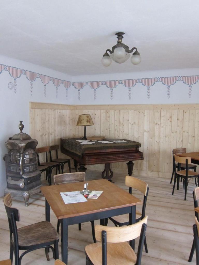 Große Gaststube im ehemaligen Gasthaus zur Hinterbrühl in Marbach an der Donau, mit Flügel, historischem Ofen, heller Holzlamperie und Kaffeehausbestuhlung.